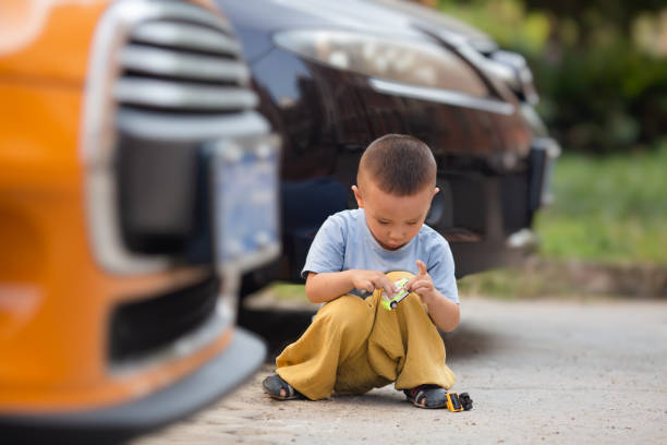 Isolated on white curly blond boy playing with cars on the gray table 