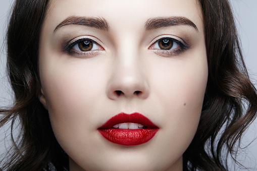 Closeup studio shot of a beautiful teenage girl with bold make up, posing against a grey background