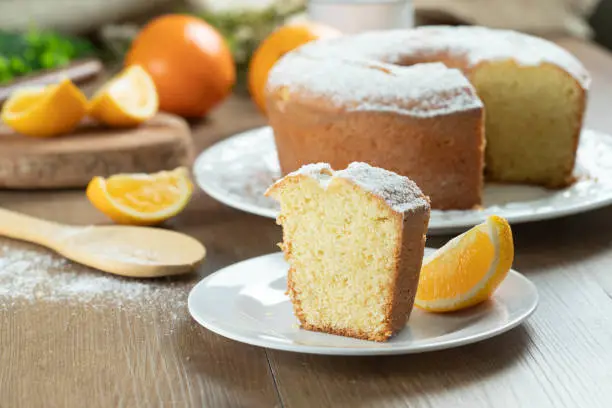 Photo of Close up piece of moist orange fruit cake on plate with orange slices on wooden table. Delicious breakfast, traditional English tea time. Orange cake recipe.