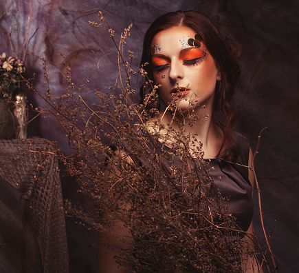Beauty and art concept: Young woman with bright make up with dry branches, studio shoot