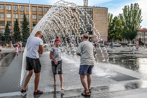 Mykolaiv, Ukraine - July 25, 2020: Arched fountain on the square near the Mykolaiv City Council on a summer evening. Adults and children have fun among the jets of water