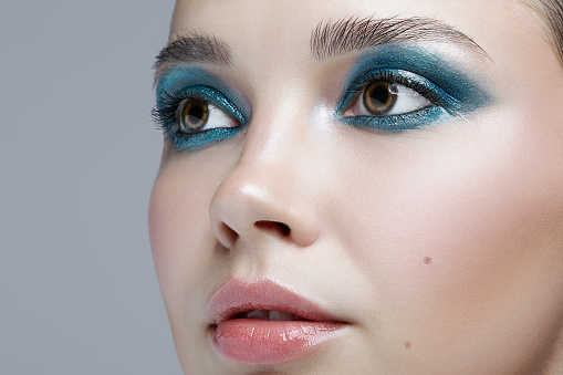 Closeup macro portrait of female face. Woman with evening beauty makeup. Girl with perfect skin and blue-green smoky eyes eye shadows