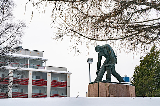 Rovaniemi, Finland - March 18th, 2022: A Bronze statue of a lumberjack debarking a log, on a snowy day in Rovaniemi, Finland.