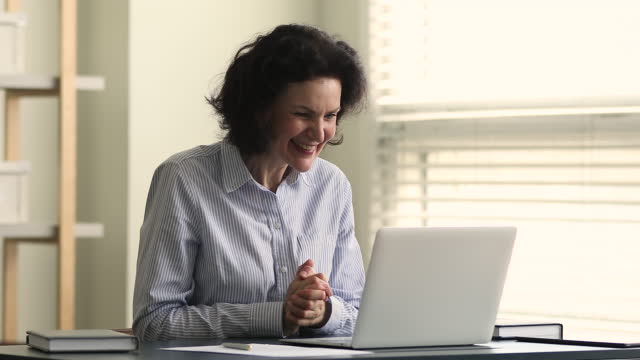 Excited aged female employee passed tests online successfully using laptop
