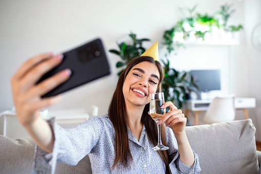 Virtual Party. Happy young woman in hat having video conference online meeting with friends and family, holding glass of wine, toasting and celebrating birthday, staying at home