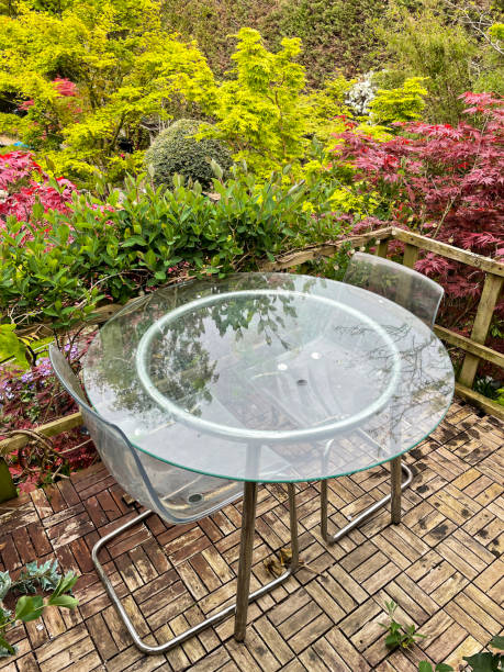 nahaufnahme des gartenbaumhauses terrassenplattform balkon mit blick auf den modernen garten hinter dem haus, glasterrassentisch und plexiglasstühle, teakholzterrasse gefliest im freien essbereich, fokus auf vordergrund - patio wood formal garden deck stock-fotos und bilder