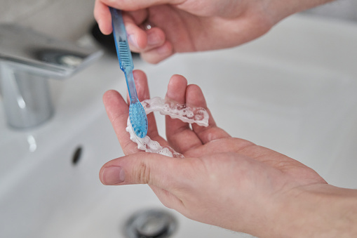 Washing and removing organic residues with toothbrush and soap from orthodontic invisible braces. Cleaning tooth aligners.