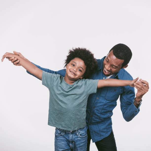 Happy handsome African American man and little boy, father and son wearing casual white t shirts giving fist bump, standing isolated on beige background. Concept of advertisement, childhood, parenthood