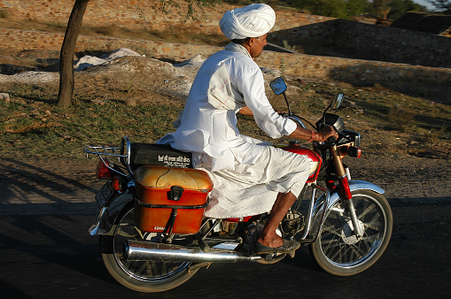 Rajasthan, India - February 21, 2006: Rajasthani farmer riding a motorbike on a country road