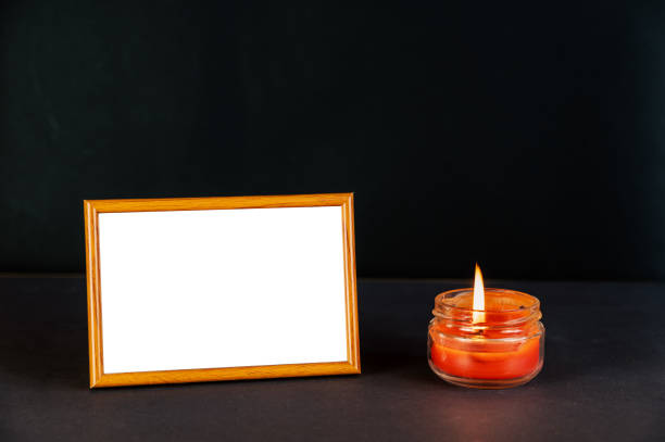 istock A beige empty photo frame against a black surface next to a burning candle. Red Lighted candle in a clear glass jar. Horizontal placement of rectangular photo frame with thin frame. 1394553372