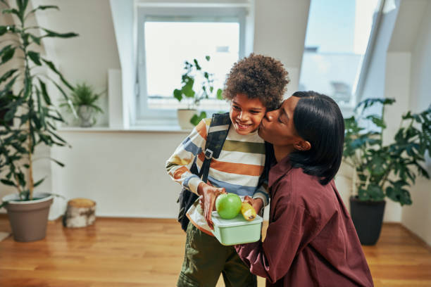 Mother kissing her son who is going to school African mother giving lunch box to her schoolboy and kissing him lunch box photos stock pictures, royalty-free photos & images
