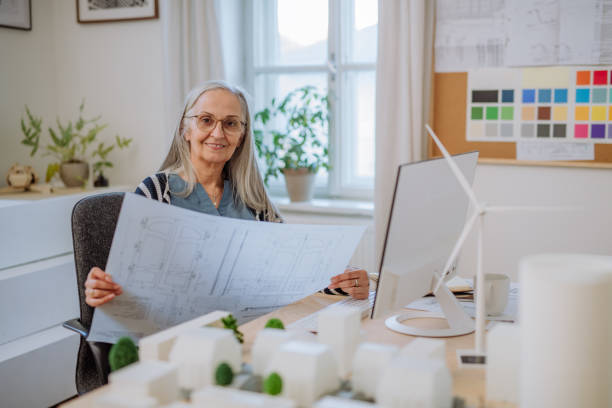 istock Senior woman eco architect with blueprints working on lapotp in office. 1394563692