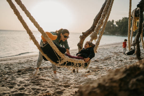 Young mother swinging little daughter and son in beach hammock at sunset