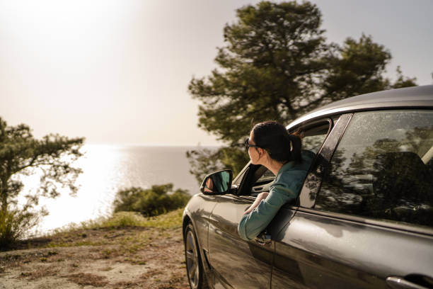 Young woman looking out the car window at sunset above the sea