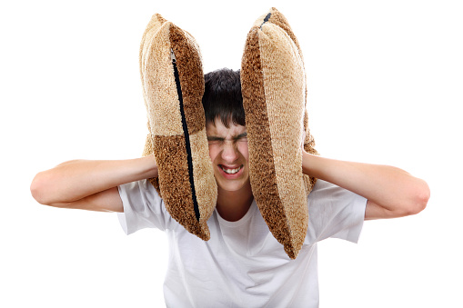 Displeased Teenager covering his Ears with Cushion Isolated On The White Background