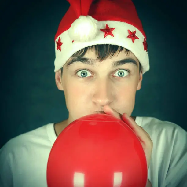 Toned Photo of Teenager in Santa Hat inflate Red Balloon On the Dark Background
