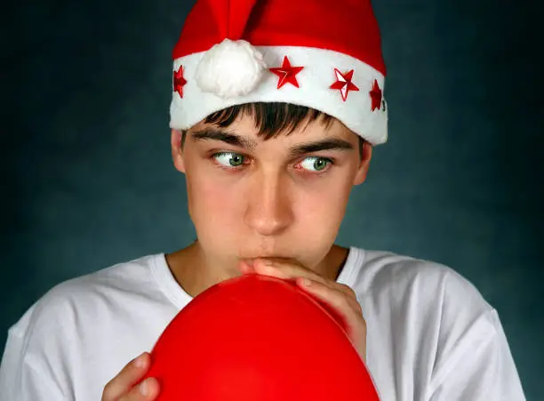 Teenager in Santa's Hat inflate a Red Balloon