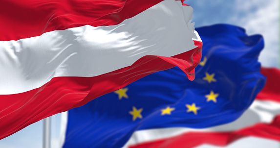 Detail of the national flag of Austria waving in the wind with blurred european union flag in the background on a clear day. Democracy and politics. European country. Selective focus.