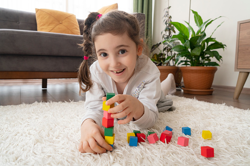 Cute little girl playing with colorful blocks at home