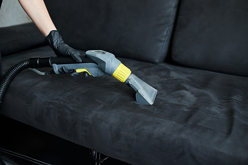Cleaning service company employee removing dirt from furniture in flat with professional equipment. Female housekeeper arm cleaning sofa with washing vacuum cleaner close up