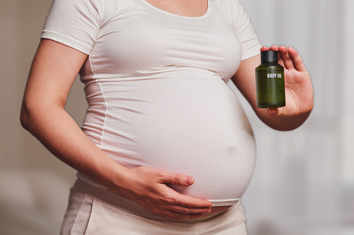 Bottle with body oil in pregnant woman, home living room