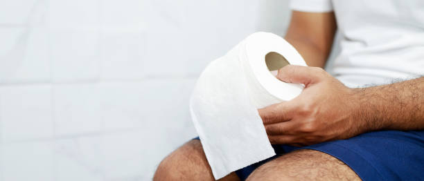 Man suffers from diarrhea hand hold tissue paper roll in front of toilet bowl. constipation in bathroom. Treatment stomach pain and Hygiene, health care stock photo