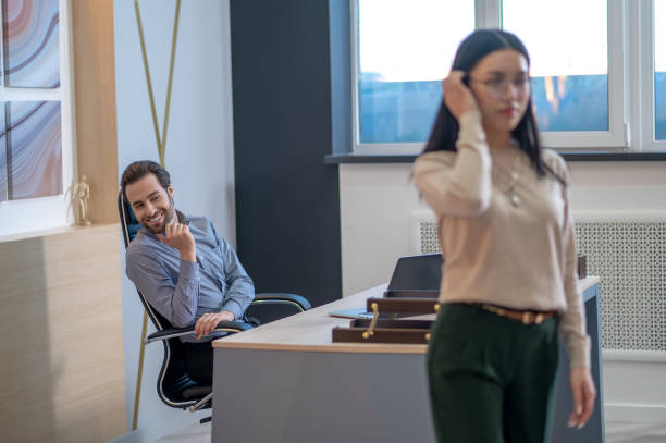 Pleased young boss staring after his secretary Smiling company director seated at the table watching his female personal assistant leaving his office work romance stock pictures, royalty-free photos & images