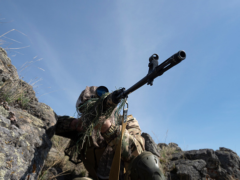 An ambush in mountains - professional special forces sniper during a special operation aiming at the enemy. Concept of modern military operations and a special operation on enemy territory.