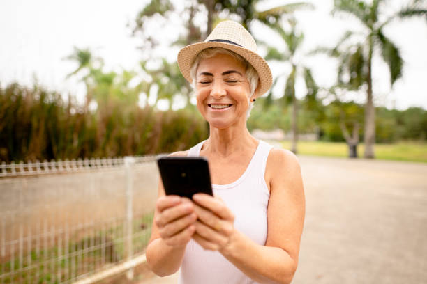 istock Mature woman reading a cellphone text while walking in a park 1394605313