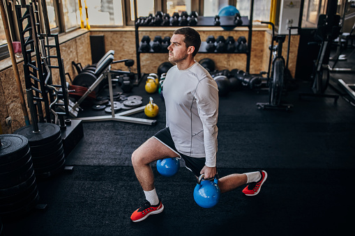 One man, fit young man training with kettlebells in gym alone.