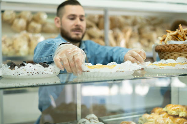 istock Bakery employee arranging cakes on display tray at counter 1394606503