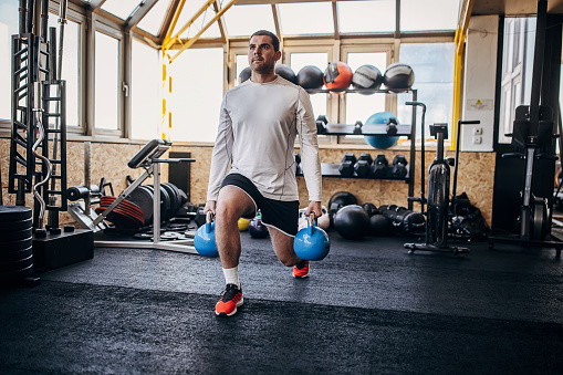 One man, fit young man training with kettlebells in gym alone.