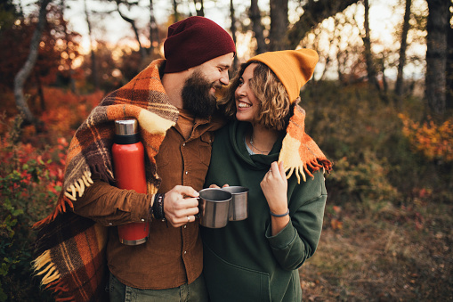 Happy couple in love drinking tea from thermos in beautiful autumn forest. Romantic fall picnic.