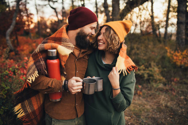 happy couple in love drinking tea from thermos in beautiful autumn forest. - roupa morna imagens e fotografias de stock