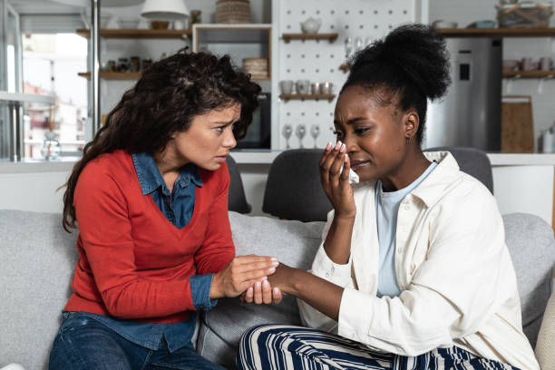 Young African American woman being victim of racism crying to her friend. Teenage female girl crime victim robed on the street. stock photo