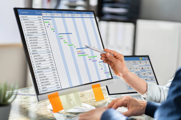 Young Businesspeople Analyzing Gantt Chart And Calendar On Computer In Office