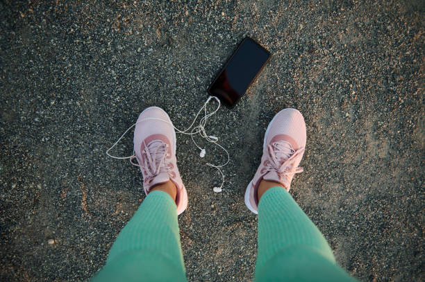 istock Top view of a black smartphone with copy ad space for advertising text or mobile app, earphones lying down on a sportsground near female athlete legs 1394634917