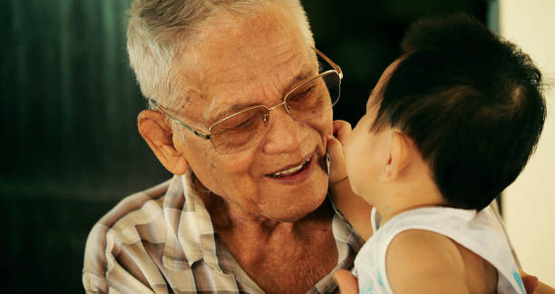 primer plano del feliz bisabuelo asiático de 80 años con una hermosa sonrisa mirando a su bisnieto bebé tocando su rostro mostrando verdadero amor y felicidad. el vínculo entre las generaciones familiares. - great grandson fotografías e imágenes de stock