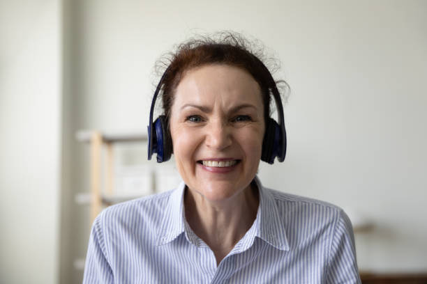 happy older business lady in head phones looking at camera - gesprek coaching detail stockfoto's en -beelden