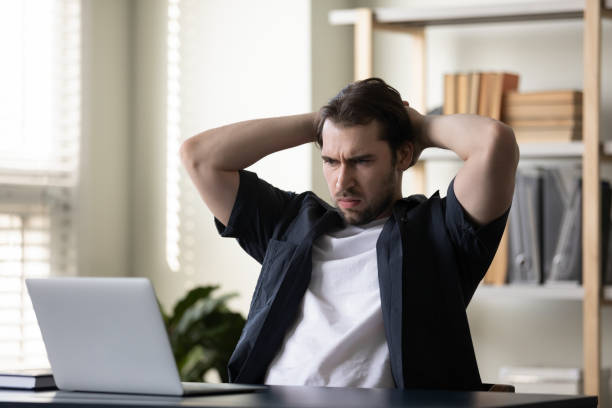 Frowning dissatisfied laptop user concerned, worried about problems Frowning dissatisfied laptop user concerned, worried about problems with computer. Angry annoyed man staring at computer screen, getting bad news, surprise, feeling stress about software, app email scam stock pictures, royalty-free photos & images