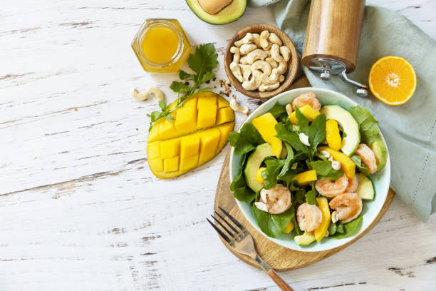 Vegetarian vegan healthy food. Salad with arugula, mango, avocado, shrimp, pecans and dressing of olive oil, honey and wine vinegar on a white rustic kitchen table. Top view, flat lay background. Copy space. comida vegetariana vegana saludable. ensalada con rúcula, mango, aguacate, camarones, nueces pecanas y aderezo de aceite de oliva, miel y vinagre de vino en una mesa blanca rústica de la cocina. vista superior, fondo plano. espacio de copia.