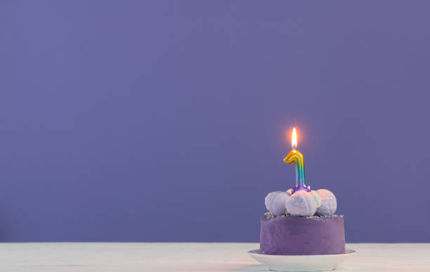 purple birthday cake with burning candles on purple  background stock photo
