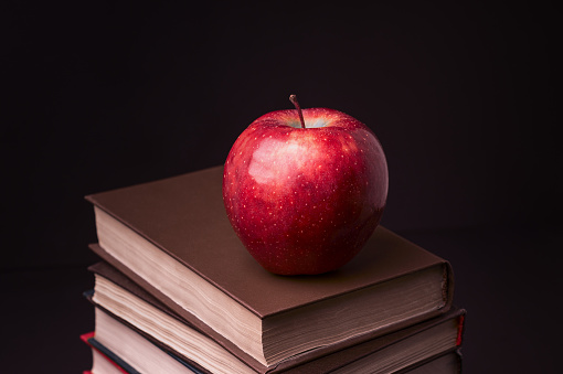 Red apple on book stack on black background