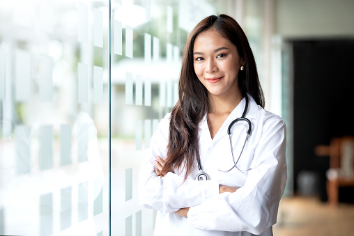 Smiling Asian female doctor in lab coat with arms crossed against looking at camera.