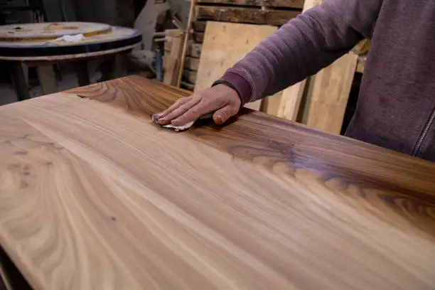Closeup of carpenter coating a wooden table with protective flaxseed oil. Process of making a wood table