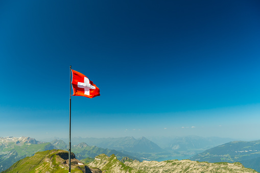 The Swiss flag waves in the wind on a mountain.
