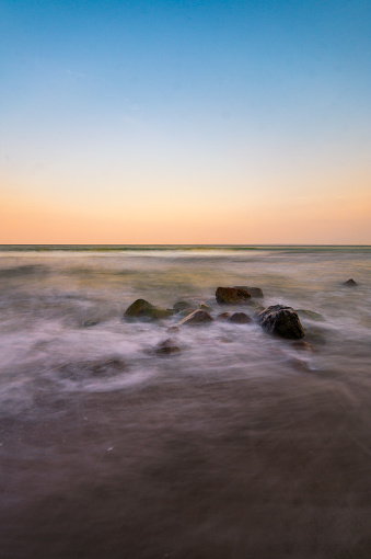 Colorful image of the sunset and the waves of the baltic sea crashing in some rocks.
