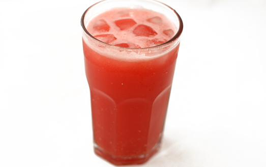 A glass of fresh watermelon smoothie juice drink, selective focus of cold melon smoothies drink in a glass with ice cubes isolated on a white background, summer tropical drinks concept