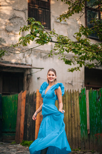 Beautiful young woman walking and exploring old city and wearing blue long dress