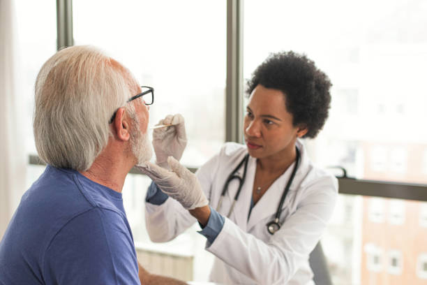 Doctor examine patient throat with spatula Female african american doctor using inspection spatula to examine older patient throat. Doctor doing throat exam of a older man who open his mouth wide doctor utensils stock pictures, royalty-free photos & images